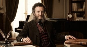 Composer Jacques Offenbach Bearded man,Jacques Offenbach, in 19th-century attire seated at a desk with leather-bound books, quills, and a grand piano in the background - image for video